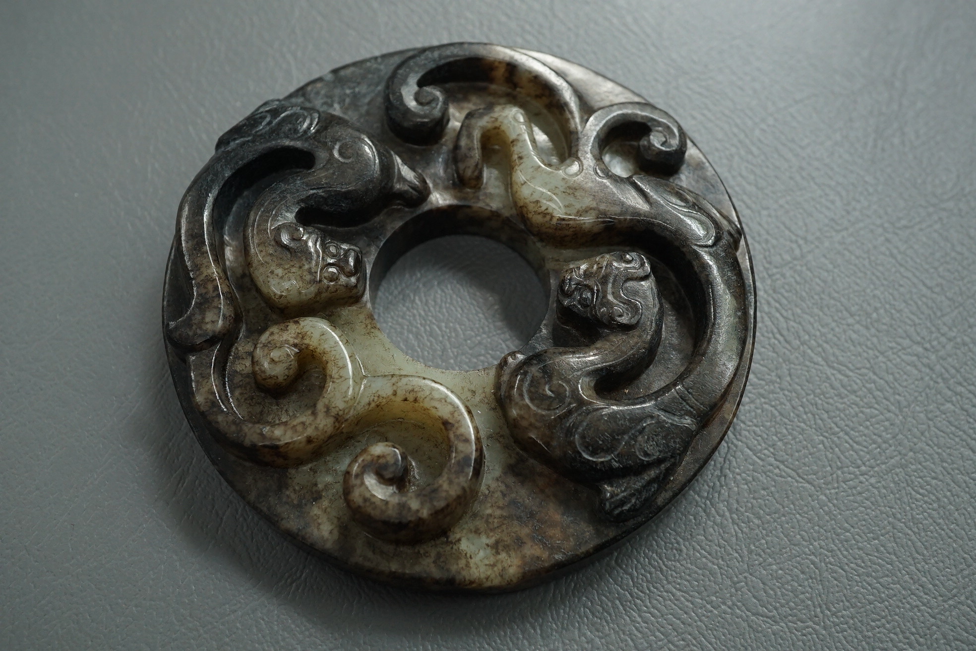 A Chinese pale celadon and black jade bi disc